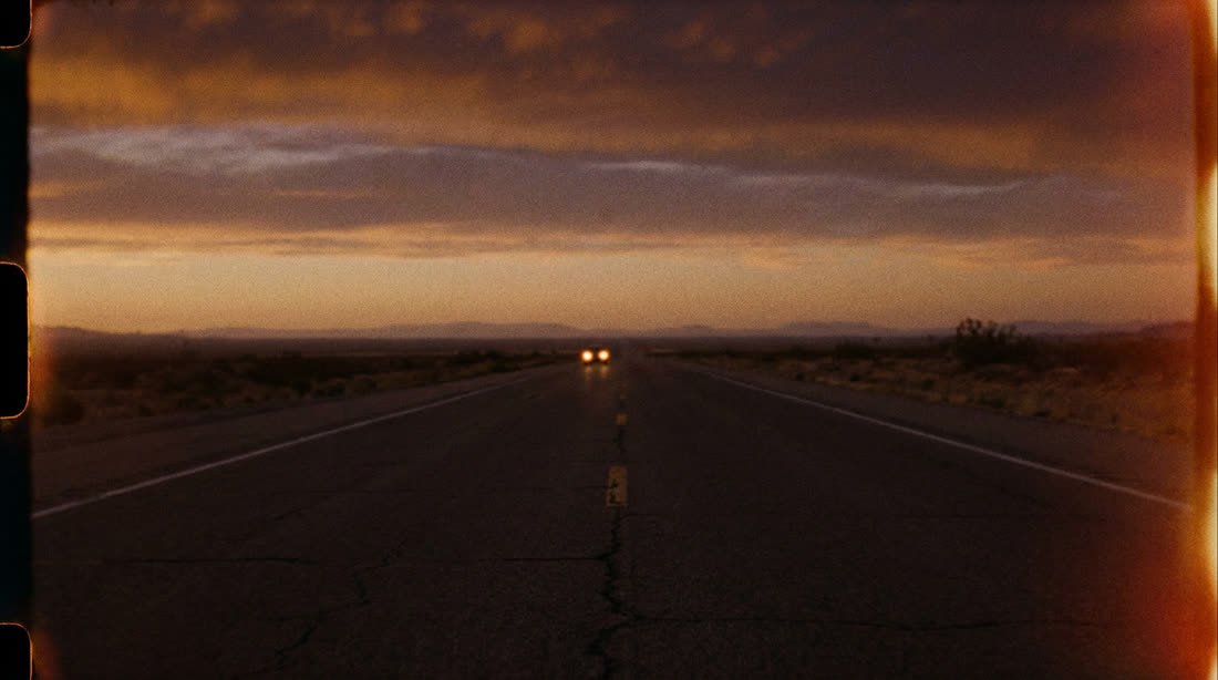 An empty desert highway at dusk under a wide sky